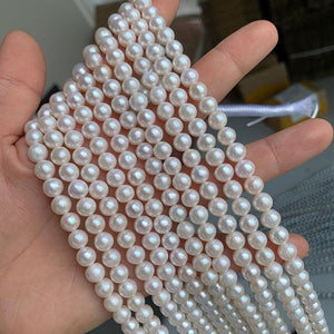 A person holding multiple strands of round freshwater pearls in white color.