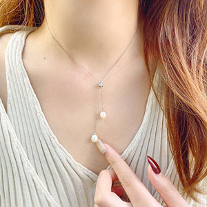 A close-up image of a person wearing a long tassel double bead necklace with pearl beads.