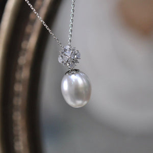 A sterling silver pendant with a central pearl surrounded by a cluster of smaller clear crystals, suspended from a silver chain.