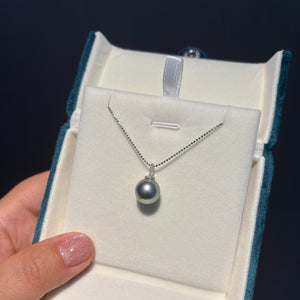 Pearl necklace in a jewelry box held by a hand against a dark background